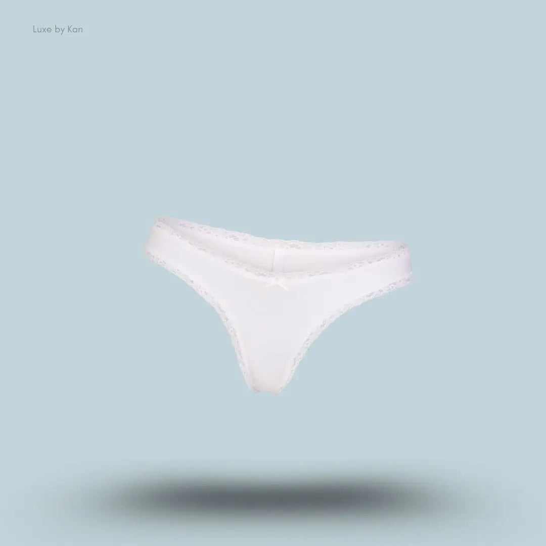 SKIMS Lightweight Cotton Lace Thong in Snow, flat lay on light blue background