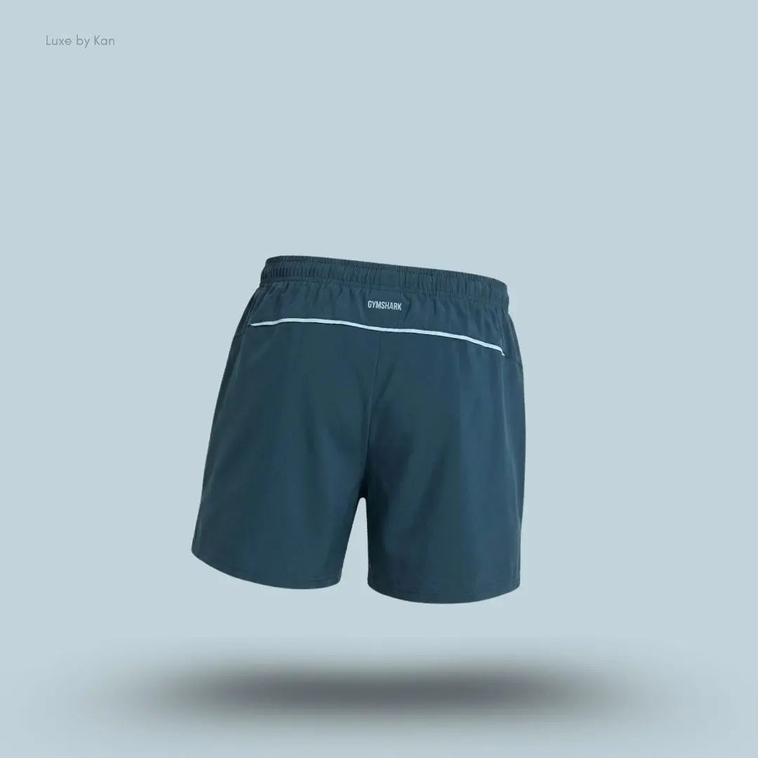 Gymshark Arrival Contrast Shorts in stealth blue displayed on a blue background with a slim-fit athletic shorts design back view
