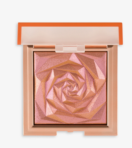 A shiny, rose-patterned nymph blush compact by huda beauty with pink and bronze shade, encased in a light orange and clear compact.